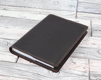 Könnte beinhalten: Ein dunkelbrauner Notizbuchumschlag aus Leder mit sichtbaren Nähten an den Rändern. Der Umschlag ist rechteckig und hat eine glatte, matte Oberfläche, die einen Stapel weißer Papierseiten umschließt, die an der Seite sichtbar sind.