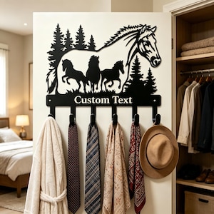 May include: A black metal wall-mounted hook rack featuring a silhouette of a large horse head and three smaller horses running in front of pine trees. The horizontal bar below the horses includes the text Custom Text and six black hooks.