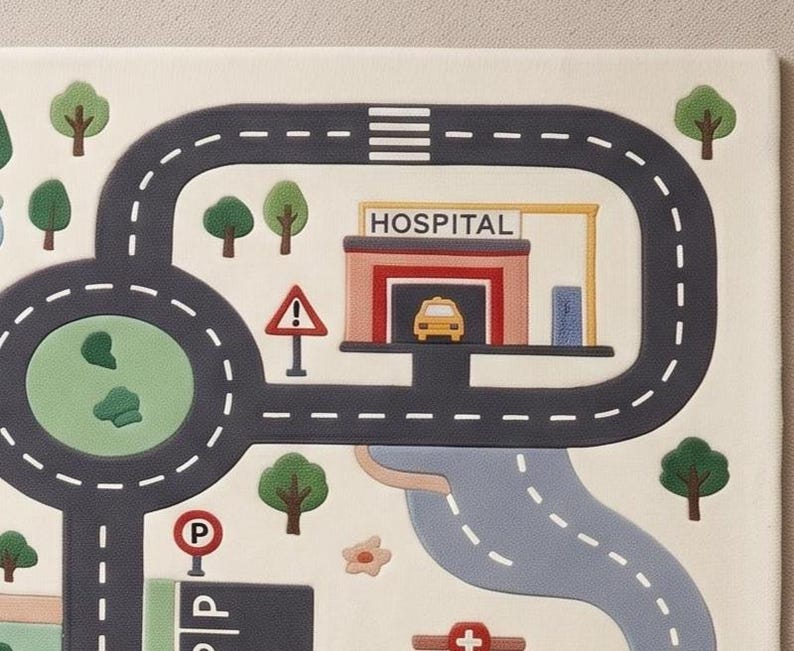 May include: A play mat featuring a printed city map with dark gray roads, white dashed lane markings, a hospital building with a yellow car, green trees, a parking sign, and a triangular warning sign on a light cream-colored background.