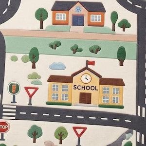 May include: A play mat featuring a town scene with dark gray roads, white lane markings, and green trees. A yellow building labeled SCHOOL with a clock and red flag sits alongside a brown house. Traffic signs include a red STOP sign and yield signs.
