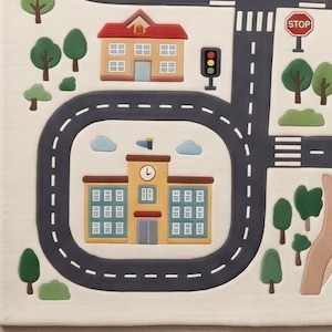 May include: A cream-colored play rug featuring a printed city map with dark gray roads, white dashed lane markings, and a red stop sign. The design includes a yellow school building with a clock, a tan house with a red roof, green trees, and bushes.