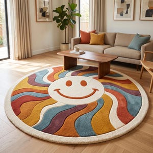 May include: A large circular area rug featuring a central cream-colored smiley face with orange eyes and a curved mouth. The design includes radiating wavy bands in shades of mustard yellow, terracotta orange, deep purple, and muted blue.