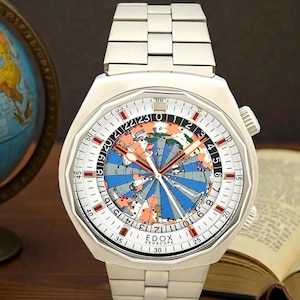 Puede incluir: Un reloj de pulsera Edox Geoscope en tono plateado con una esfera de mapa mundial multicolor, escala de 24 horas, manecillas luminosas y brazalete de eslabones de acero inoxidable. La esfera muestra una proyección central con océanos azules.