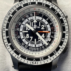 May include: A Fortis wristwatch with a black dial, white numerals, and a rotating slide rule bezel. The watch features luminous hands, an orange second hand, and a black rubber strap. The dial displays the Fortis logo and Swiss Made text.