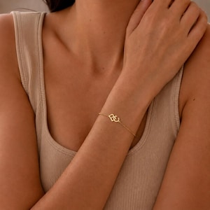 May include: A delicate gold bracelet with a linked heart design. The bracelet has a thin chain and a small, heart-shaped charm. The jewellery is worn on a wrist, highlighting its minimalist style and subtle shine. The chain is approximately 18 cm long.