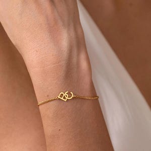 Puede incluir: Pulsera de cadena dorada con un dije en forma de coraz&oacute;n. El dije presenta las letras entrelazadas "B" y "C". Una joya delicada.