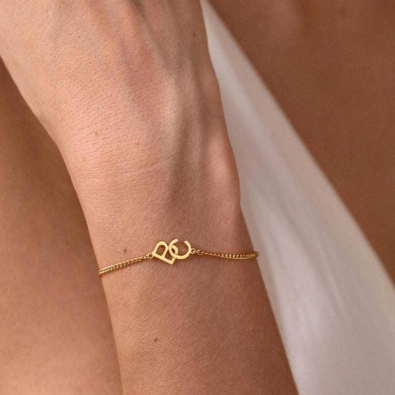 Puede incluir: Pulsera de cadena dorada con un dije en forma de coraz&oacute;n. El dije presenta las letras entrelazadas "B" y "C". Una joya delicada.
