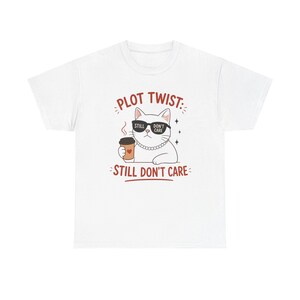 Puede incluir: Camiseta blanca con un diseño de gato de dibujos animados. El gato lleva gafas de sol y un collar de perlas, sosteniendo una taza de café. El texto de la camiseta dice "PLOT TWIST: STILL DON'T CARE" en marrón. El diseño incluye estrellas y vapor.