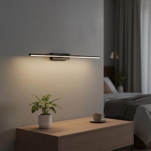 以下が含まれることがあります： モダンな黒い壁掛け照明器具。線状のLED光源を備えています。灰色の壁に取り付けられ、木製のナイトスタンドの上にあります。小さな鉢植えの植物とコーヒーカップがナイトスタンドに置かれています。