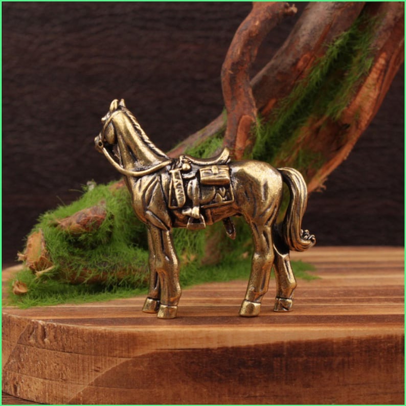 May include: A detailed bronze horse figurine with a saddle. The horse is standing on a wooden surface, with moss and a branch in the background. The figurine has intricate details, showcasing the horse's form and tack.