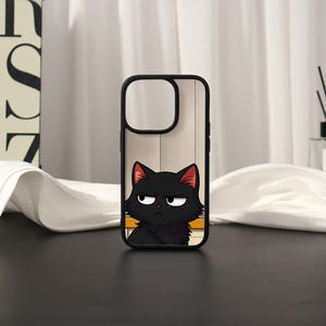 May include: A black phone case featuring a graphic illustration of a grumpy black cat with large white eyes and pink inner ears. The cat is positioned at the bottom of the case against a light-coloured background with a horizontal yellow stripe.