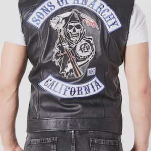 May include: Black leather vest with a large patch featuring a skull with a scythe, the words "Sons of Anarchy" and "California". The vest is sleeveless and has a classic biker style.