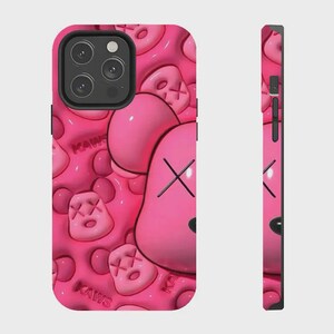 K&ouml;nnte beinhalten: Eine leuchtend pinke Smartphone-H&uuml;lle mit einem wiederkehrenden gepr&auml;gten Muster aus KAWS-Charakterk&ouml;pfen mit X-f&ouml;rmigen Augen und dem Schriftzug KAWS in Reliefoptik. Das Design umfasst einen schwarzen Kameraausschnitt und seitliche Tasten.