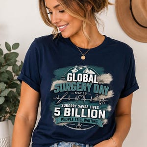 Könnte beinhalten: Marineblaues T-Shirt mit dem Text "GLOBAL SURGERY DAY - MAY 25". Das Shirt zeigt auch den Text "SURGRRY SAVES LIVES 5 BILLION PEOPLE STILL WAITING" in Weiß und Türkis. Das T-Shirt wird getragen.