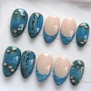 Peut inclure: Dix faux ongles avec différents motifs. Certains ongles présentent un effet marbré bleu et turquoise avec de petits accents roses. D'autres ont une base nude avec un motif de vagues bleues sur le bout. Les ongles sont de forme ovale.