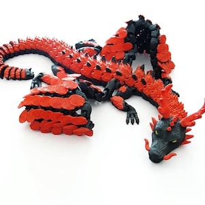 Könnte beinhalten: Detaillierte, bewegliche Drachenskulptur in Rot und Schwarz. Der Drache hat einen langen, segmentierten Schwanz, strukturierte Schuppen und einen detaillierten Kopf mit Hörnern. Die Skulptur steht auf einer weißen Oberfläche.
