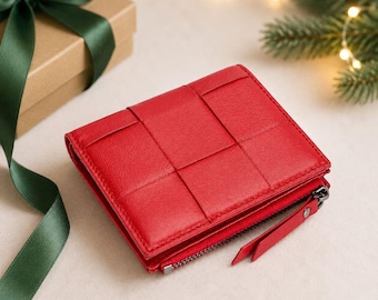 May include: A bright red bi-fold wallet featuring a woven grid pattern on the exterior surface. The wallet includes a side zipper closure with a matching red leather pull tab and dark metal hardware, showcasing a structured and compact design.