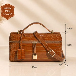 May include: A brown crocodile-embossed leather handbag with a top handle, a detachable shoulder strap, and a gold-tone padlock closure. The bag measures 23 inches wide, 12 inches high, 7 inches deep, with a 4.5-inch handle drop. Features a leather tag.