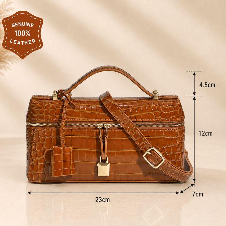 May include: A brown crocodile-embossed leather handbag with a top handle, a detachable shoulder strap, and a gold-tone padlock closure. The bag measures 23 inches wide, 12 inches high, 7 inches deep, with a 4.5-inch handle drop. Features a leather tag.