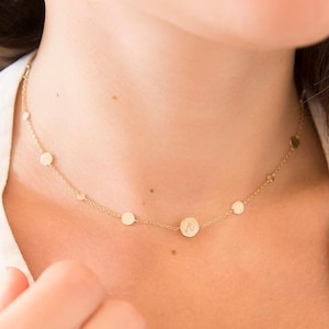 May include: A gold chain necklace with small round charms, including one with an initial "A" engraved on it.