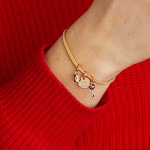 May include: Gold-toned bracelet with three charms: a padlock, a disc with "my love" engraved, and a key. The bracelet is worn on a wrist, against a red background. The padlock charm has a small diamond.