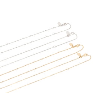 May include: Four silver and two gold beaded chain necklaces with lobster clasps. The chains are arranged in a staggered pattern, with the silver chains on top and the gold chains on the bottom.
