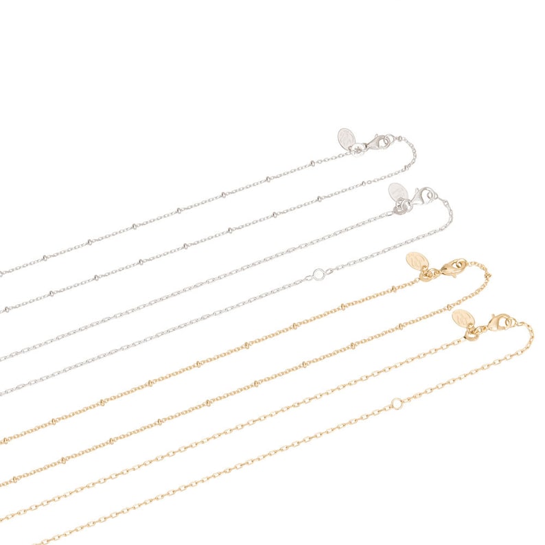 May include: Four silver and two gold beaded chain necklaces with lobster clasps. The chains are arranged in a staggered pattern, with the silver chains on top and the gold chains on the bottom.