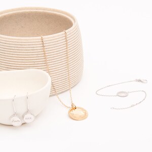 May include: A set of gold and silver jewelry featuring a necklace with a round pendant, a bracelet with a round charm, and a pair of earrings with round charms. The charms are engraved with the words "love" and "xxx".