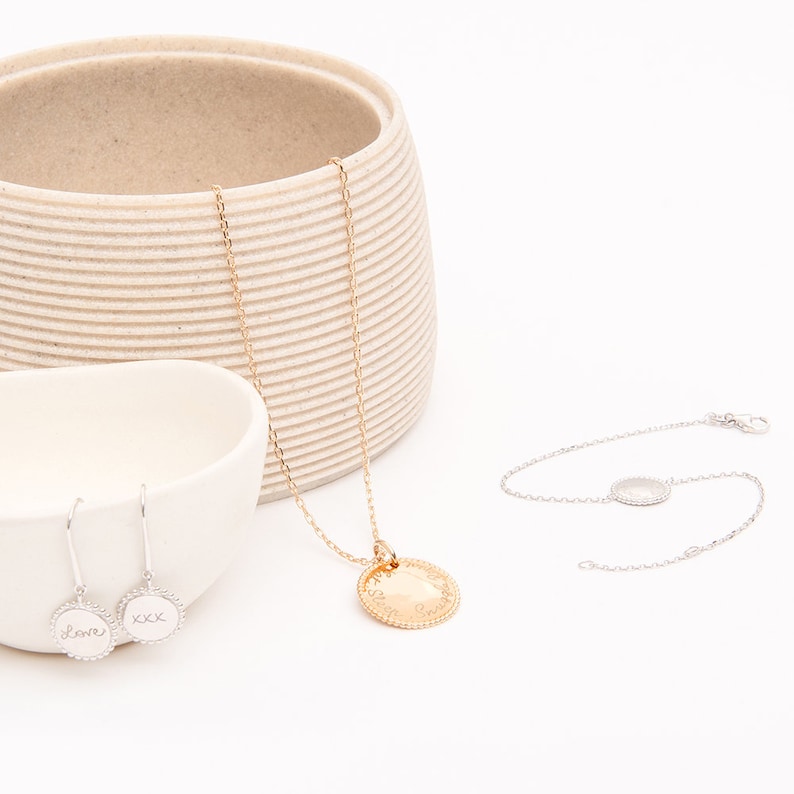 May include: A set of gold and silver jewelry featuring a necklace with a round pendant, a bracelet with a round charm, and a pair of earrings with round charms. The charms are engraved with the words "love" and "xxx".