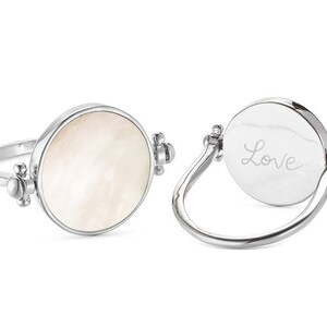 K&ouml;nnte beinhalten: Ein silberner Ring mit einem runden, wei&szlig;en Perlmuttstein auf der einen Seite und dem Wort "Love" auf der anderen Seite.