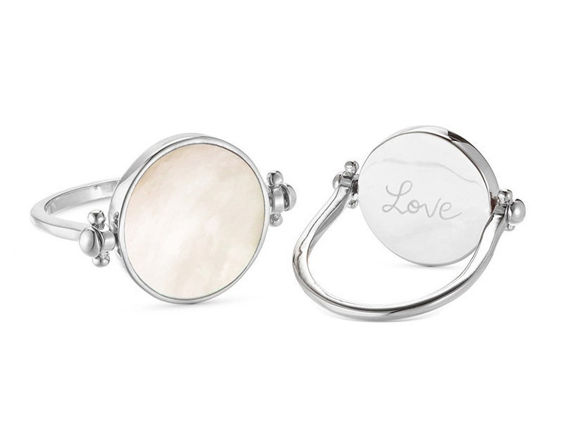 K&ouml;nnte beinhalten: Ein silberner Ring mit einem runden, wei&szlig;en Perlmuttstein auf der einen Seite und dem Wort "Love" auf der anderen Seite.
