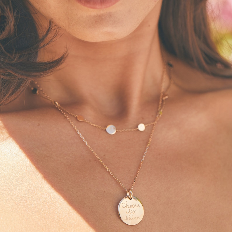 May include: Gold necklace with a round pendant that says "Choose to shine". The necklace has a delicate chain and three smaller round charms.