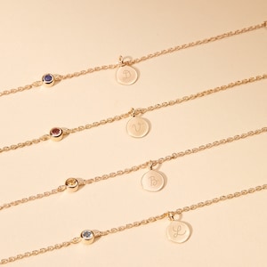 May include: Four gold chain bracelets with small gemstone charms and personalized disc charms. The charms are engraved with the letters D, V, B, and L.