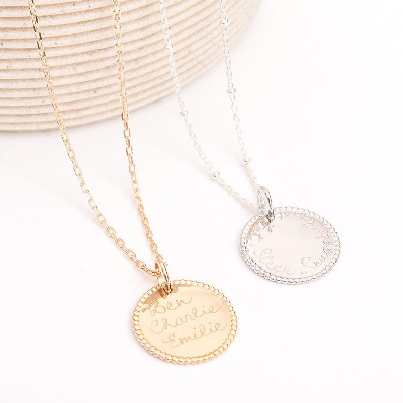 May include: Two gold and silver necklaces with round pendants. The gold pendant has the names "Ben, Charlie, & Emilie" engraved on it. The silver pendant has the text "Alex, Sleep, Charlie" engraved on it.