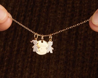 Op de afbeelding: Een gouden ketting met drie hangers. Twee hangers zijn kleine, sprankelende kinderfiguren. De derde is een gouden schijf met de inscriptie "Alice & Paul". De ketting wordt door een persoon omhoog gehouden.