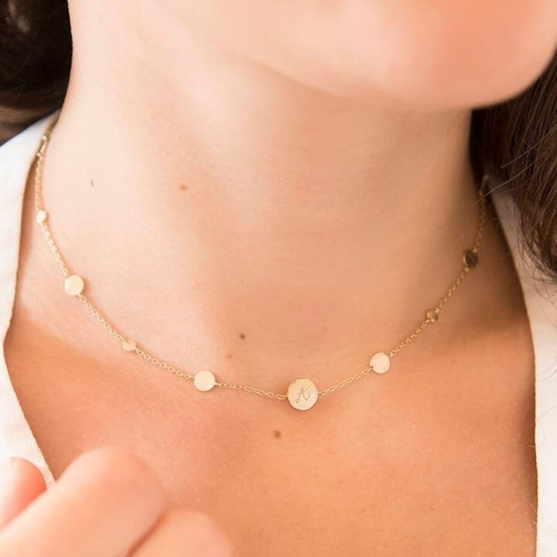 May include: A gold chain necklace with small round charms, including one with an initial "A" engraved on it.