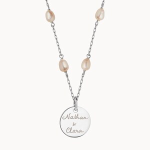 May include: Silver necklace with a round pendant engraved with "Nathan & Clara" and five small pearl accents.