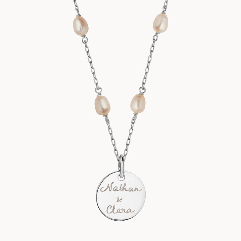 May include: Silver necklace with a round pendant engraved with "Nathan & Clara" and five small pearl accents.