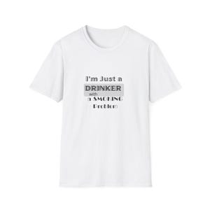 Może przedstawiać: Biały t-shirt z krótkim rękawem z czarnym napisem na klatce piersiowej o treści I'm Just a DRINKER with a SMOKING Problem. Słowo DRINKER jest wyróżnione szarym prostokątnym tłem, a cały projekt wykorzystuje przejrzystą czcionkę.