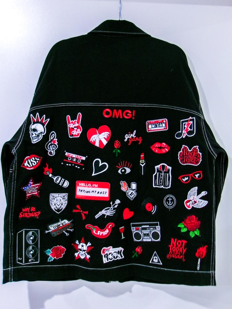 May include: A black denim jacket featuring numerous embroidered patches in red, white, and black. The patches include text like OMG!, girl gang, KISS, USA, WHY SO SERIOUS?, HELLO, I'M TRYING MY BEST, ROCK, and NOT TODAY Satan, alongside various icons.
