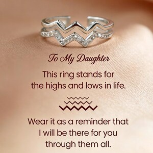 May include: A silver-toned open ring featuring a double-layered zigzag design with small clear stones embedded in the lower band. The text reads: To My Daughter, This ring stands for the highs and lows in life, Wear it as a reminder that I will be there for you through them all.