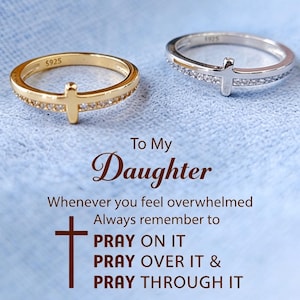 Peut inclure: Deux bagues, une dorée et une argentée, chacune avec un motif de croix et de petites pierres claires sur l'anneau. Les deux bagues portent l'inscription S925. Le texte indique : To My Daughter, Whenever you feel overwhelmed, Always remember to PRAY ON IT, PRAY OVER IT & PRAY THROUGH IT.