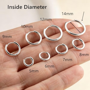Può includere: Una collezione di orecchini a cerchio color argento di varie dimensioni, etichettati con le misure del diametro interno che vanno da 5 mm a 14 mm. Il testo 'Inside Diameter' è stampato in alto, con frecce che indicano i punti di misurazione.