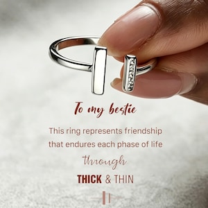 May include: A silver ring with an open design. One end has a vertical bar, the other a bar with small, clear stones. The text reads "To my bestie" and "THICK & THIN".