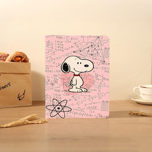 May include: A pink notebook featuring Snoopy with a red collar, set against a backdrop of mathematical equations and diagrams. A fun item for students and Peanuts fans. The notebook is a great size for carrying around.