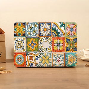 May include: A laptop protective cover featuring a grid of colorful square tiles with intricate floral and geometric patterns in shades of blue, yellow, orange, green, and white, with a central cutout revealing the silver Apple logo.