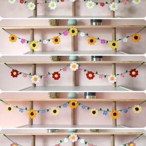 May include: A selection of crocheted flower garlands in a variety of colours, including white, yellow, orange, red, and pink. The garlands are strung on green yarn and feature different flower designs. The garlands are displayed on wooden shelves.