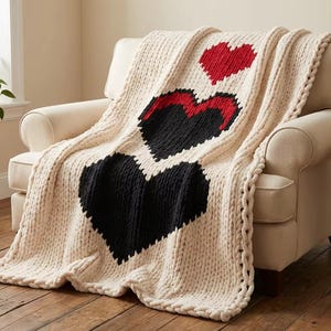 Peut inclure: Une couverture en tricot épais de couleur crème drapée sur un fauteuil beige. La couverture présente trois grands cœurs : un cœur rouge en haut, un cœur noir au milieu et un grand cœur noir en bas. Les bords de la couverture ont une bordure décorative.