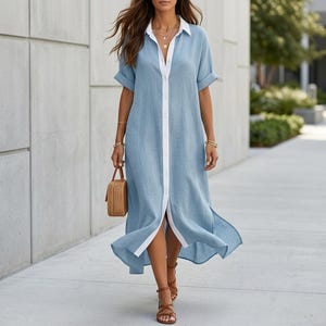 Puede incluir: Vestido camisero azul claro con ribete blanco y cierre de botones. El vestido tiene mangas cortas y cuello camisero. Un pequeño bolso de mano tejido y sandalias marrones completan el look. El vestido es hasta la rodilla.