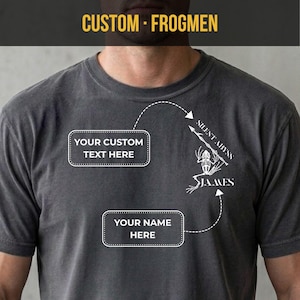 May include: Dark gray t-shirt with the text "CUSTOM - FROGMEN" at the top. The shirt features a white graphic of a frog skeleton with the words "SILENT ABYSS" and "JAMES". There are also two boxes with the text "YOUR CUSTOM TEXT HERE" and "YOUR NAME HERE".